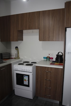 A kitchen with wooden cabinets, a white stove, a kettle, and a toaster. - By The Sea II (Limassol)