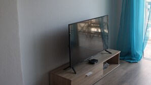 A modern room with a wooden TV stand, a mounted TV, and a shelf with decorative items. - By The Sea II (Limassol)
