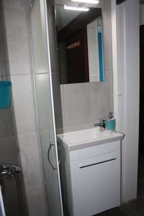 A bathroom with a white sink, a mirror, and a shower. - By The Sea II (Limassol)