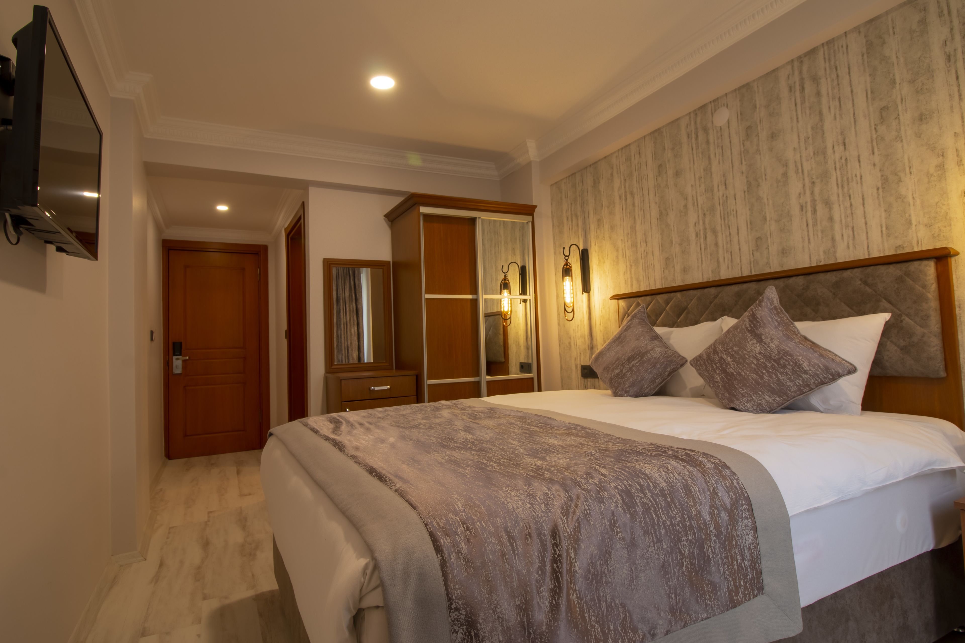 Hotelkamer met een groot bed, een kledingkast, een spiegel en een wandgemonteerde flatscreen-televisie.