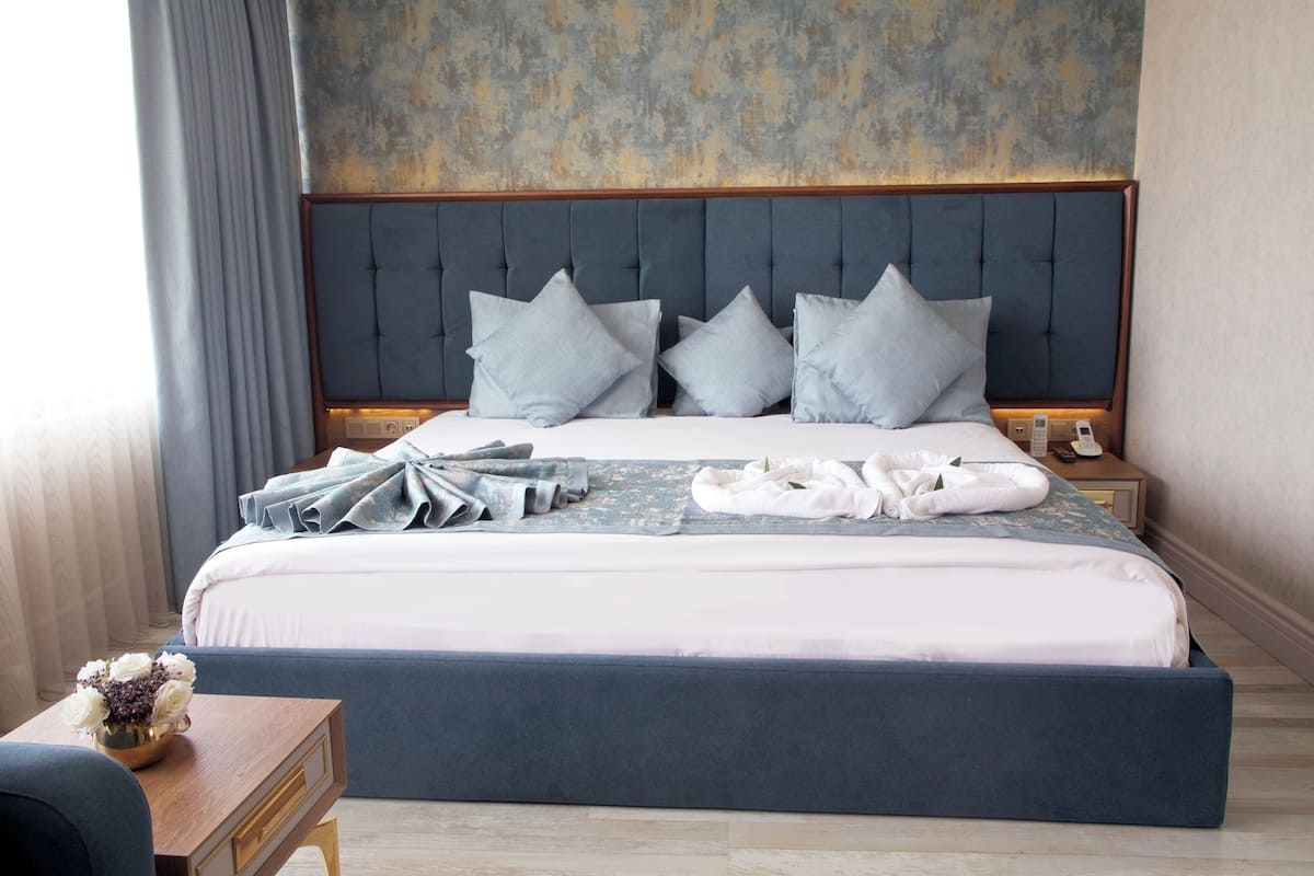 A neatly made bed with a tufted headboard, pillows, and folded towels on a wooden bedside table.