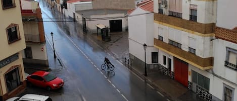 A street view with buildings, parked cars, and a cyclist.