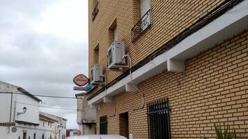 A white Peugeot car parked on a cobblestone street in front of a brick building with air conditioning units and a sign that reads "Alhambra Pension Real".