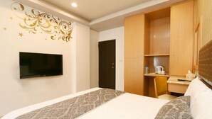 A hotel room with a bed, a TV mounted on the wall, a wooden wardrobe, and a small desk with a kettle and cup. - Yilan Jimmy Villa (Yilan)
