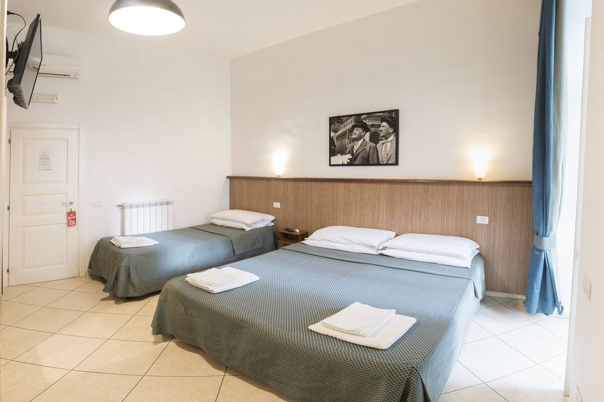 A hotel room with two beds, a wooden headboard, a framed picture on the wall, and a white door.