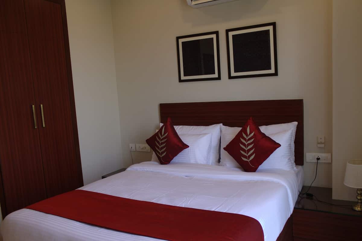 Habitación de hotel con una cama grande, dos cuadros en la pared, un armario y una mesita de noche con una lámpara.