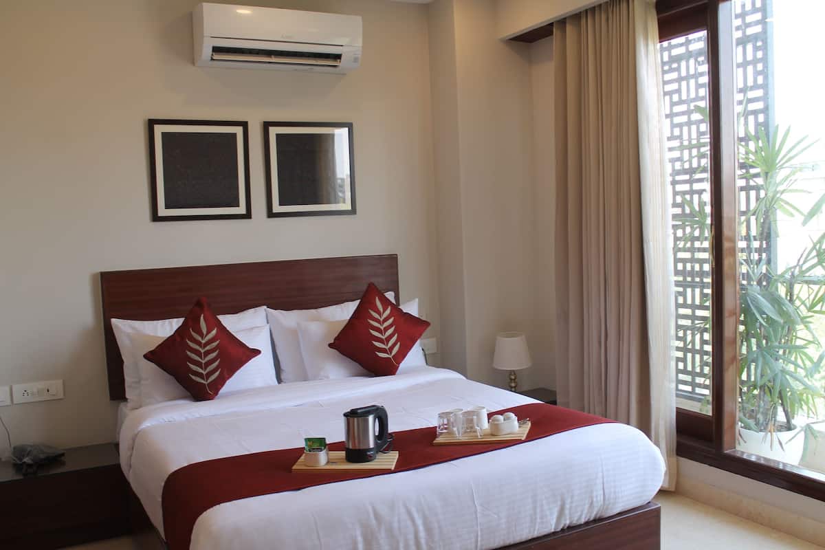 Una habitación de hotel con cama, mesita de noche, ventana con cortinas y unidad de aire acondicionado.
