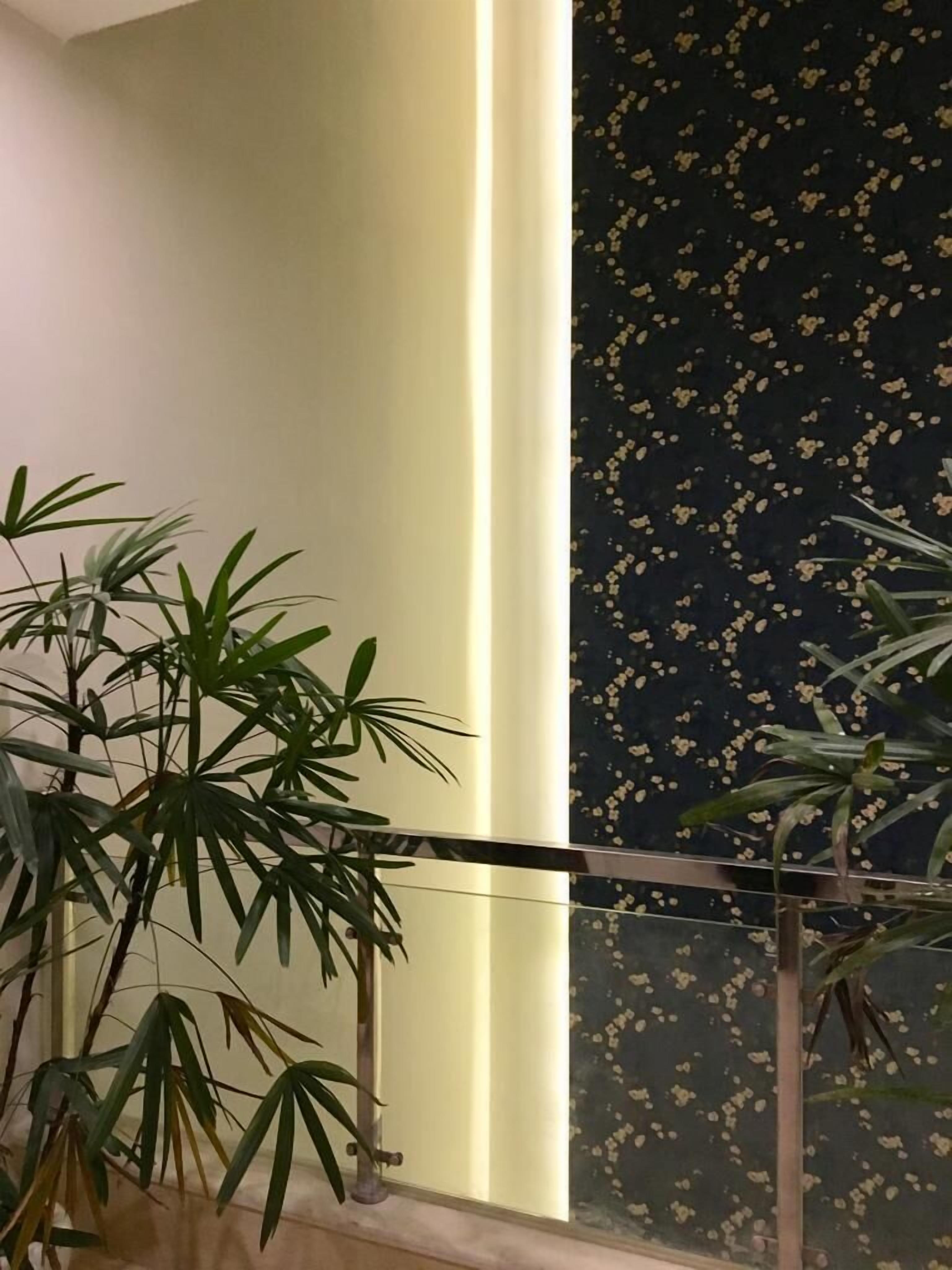 A room with a large window, a plant in the foreground, and a wall with a dark pattern.