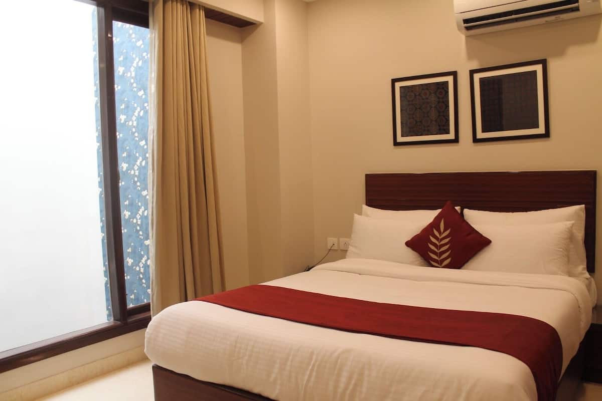 Una habitación de hotel con una cama, un ventanal con cortinas y dos cuadros en la pared.