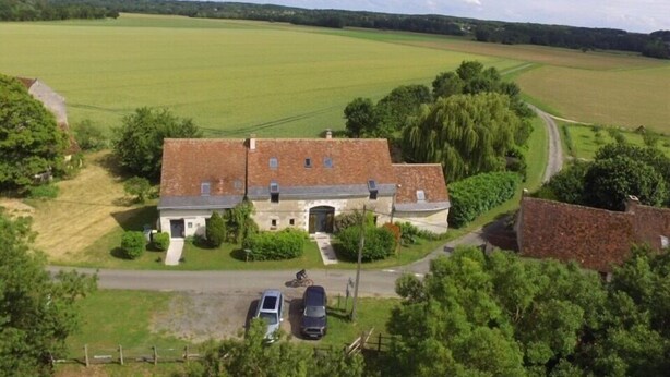 Een groot, laag gebouw met een bakstenen gevel en plat dak, omgeven door uitgestrekte groene velden en bomen.