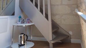Een trap met een houten balk en een witte leuning, die leidt naar een kamer met een klein tafeltje en een waterkoker.