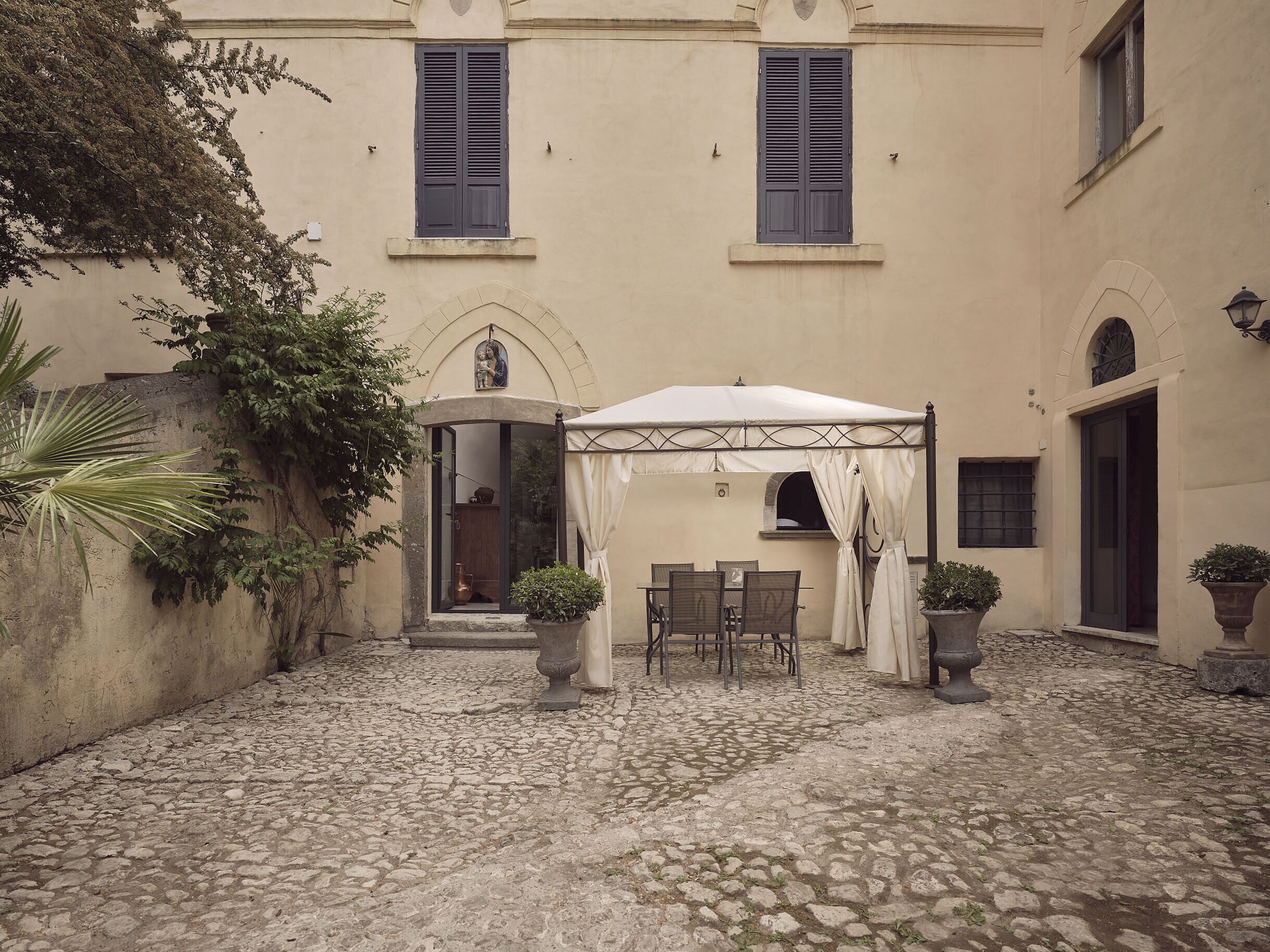 A courtyard with a covered seating area, stone flooring, and potted plants.