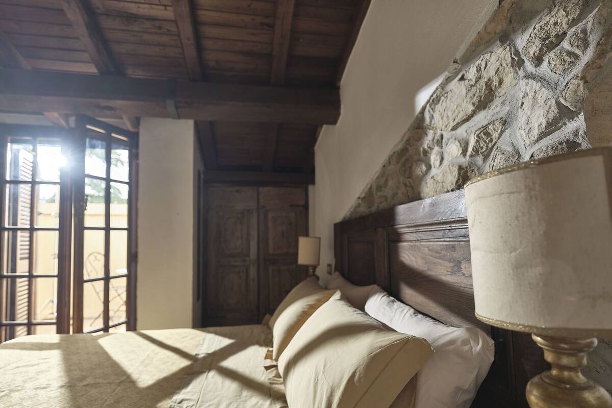 Un dormitorio con cabecera de madera, una cama con ropa de cama color beige y una lámpara sobre una mesita de noche.