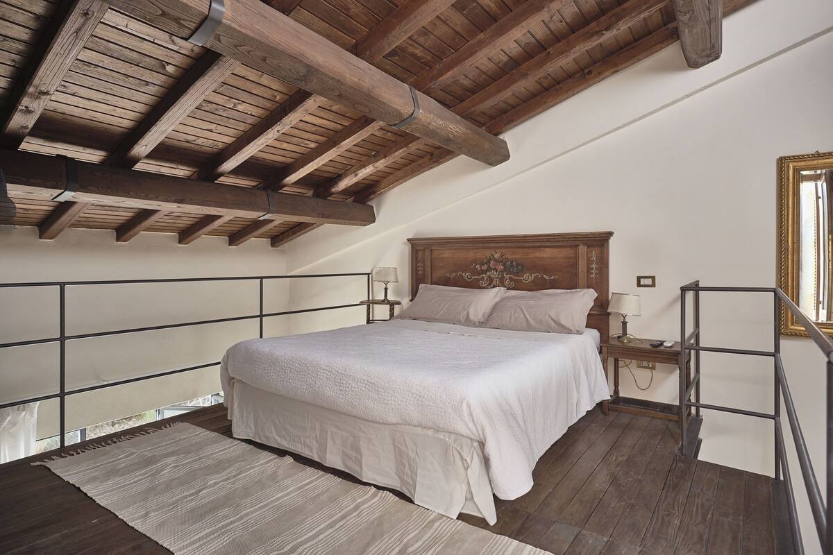 Un dormitorio con techo de madera, una cama con sábanas blancas, una mesita de noche y un ventanal con vistas.