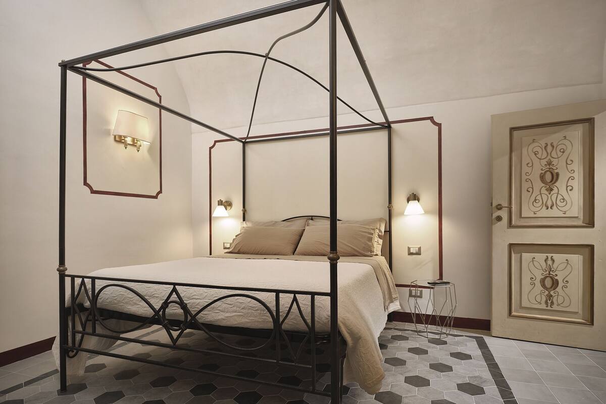 Una cama con dosel sobre un armazón metálico, dos lámparas de noche y un suelo con estampado.