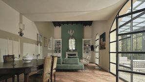 Een eethoek met een tafel, stoelen en een open haard. Er staan boekenkasten en een groot raam met uitzicht op de omgeving.