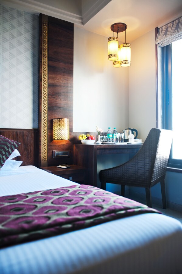 Habitación de hotel con cama, escritorio, silla, lámpara y ventana con cortinas.