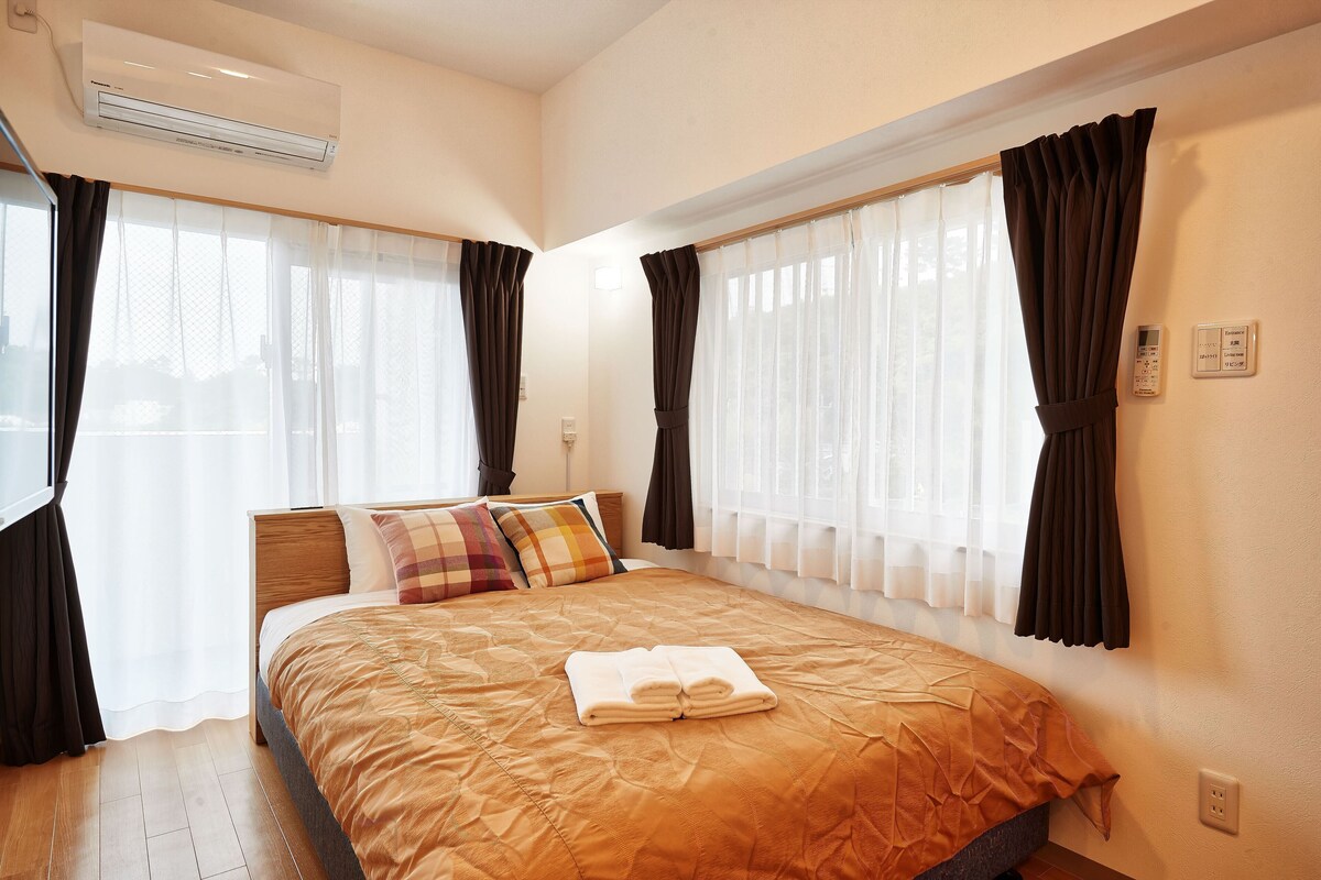 A hotel room with a bed, curtains, an air conditioning unit, and a thermostat.