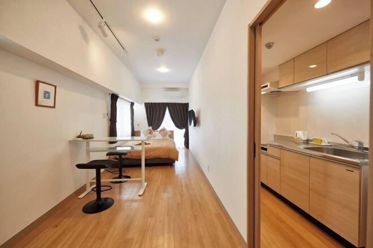 Quarto de hotel compacto com cozinha compacta, uma cama com cabeceira, uma pequena mesa com cadeira e uma janela com cortinas.