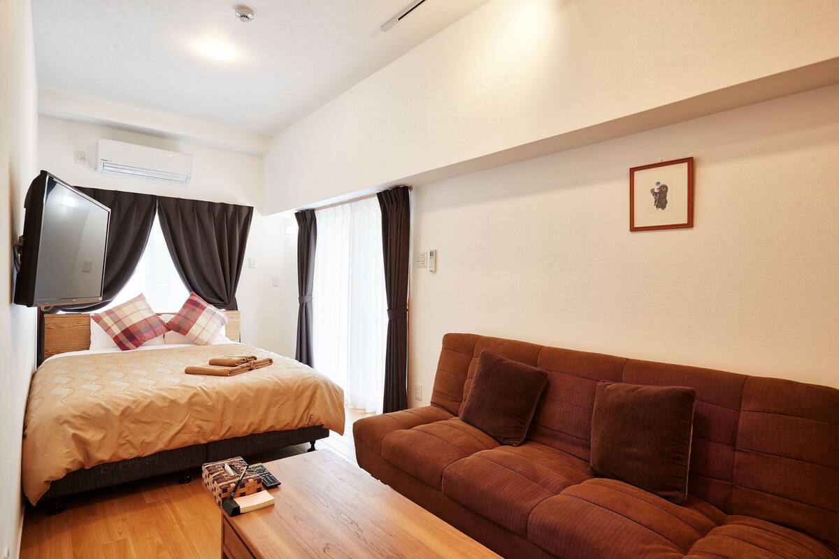 Quarto de hotel com uma cama, um sofá marrom, uma mesa de centro de madeira e uma televisão.