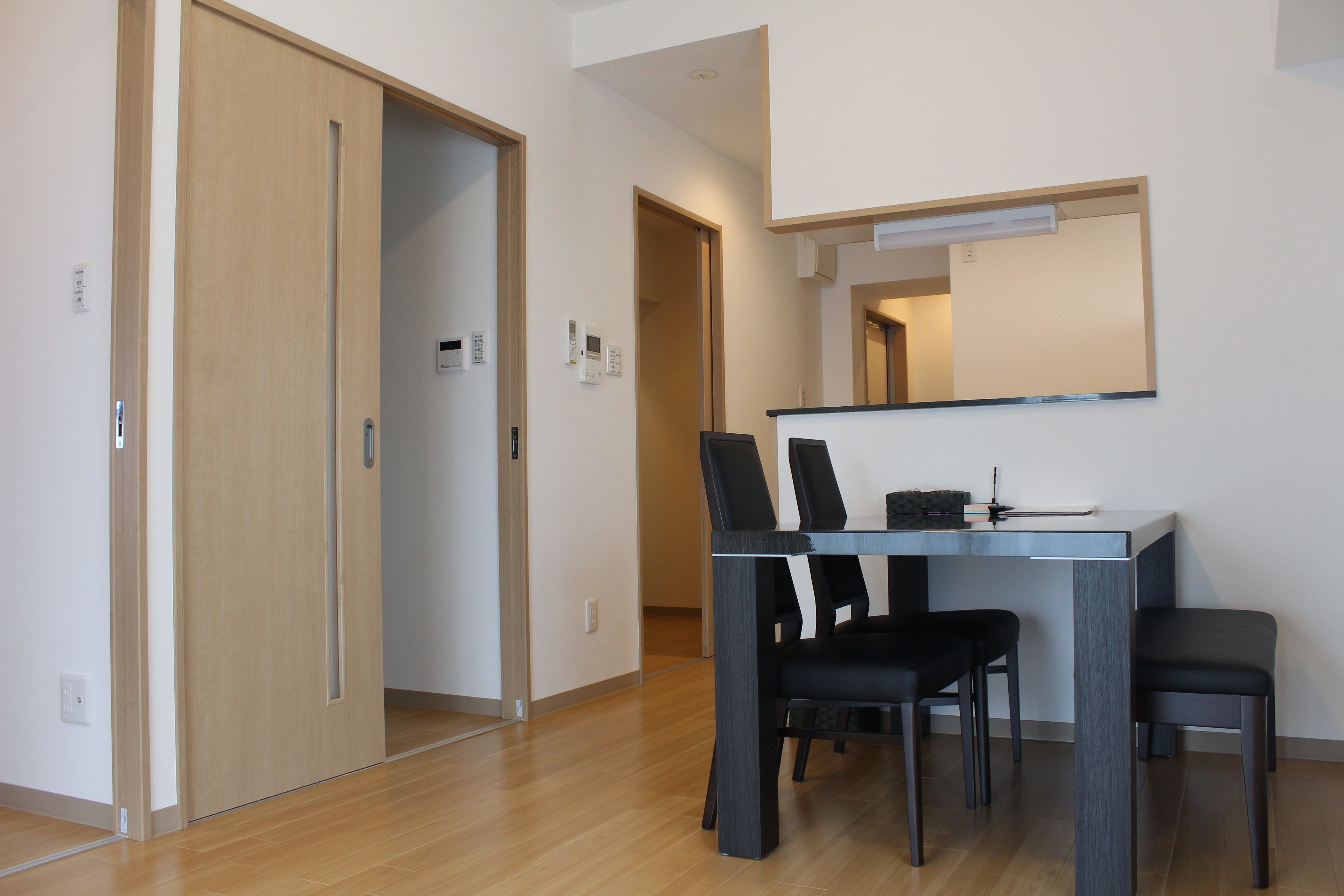 Un comedor moderno con piso de madera, una mesa de comedor con cuatro sillas y un espejo grande sobre la mesa.