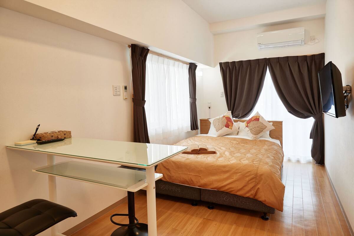 Quarto com cama, escrivaninha, cadeira e televisão.