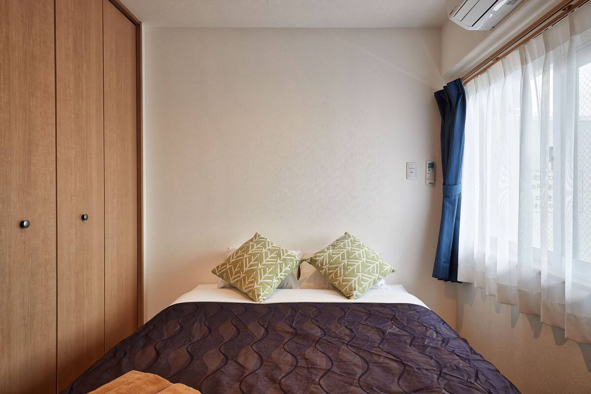 Quarto com cama, duas almofadas, guarda-roupa e janela com cortinas.