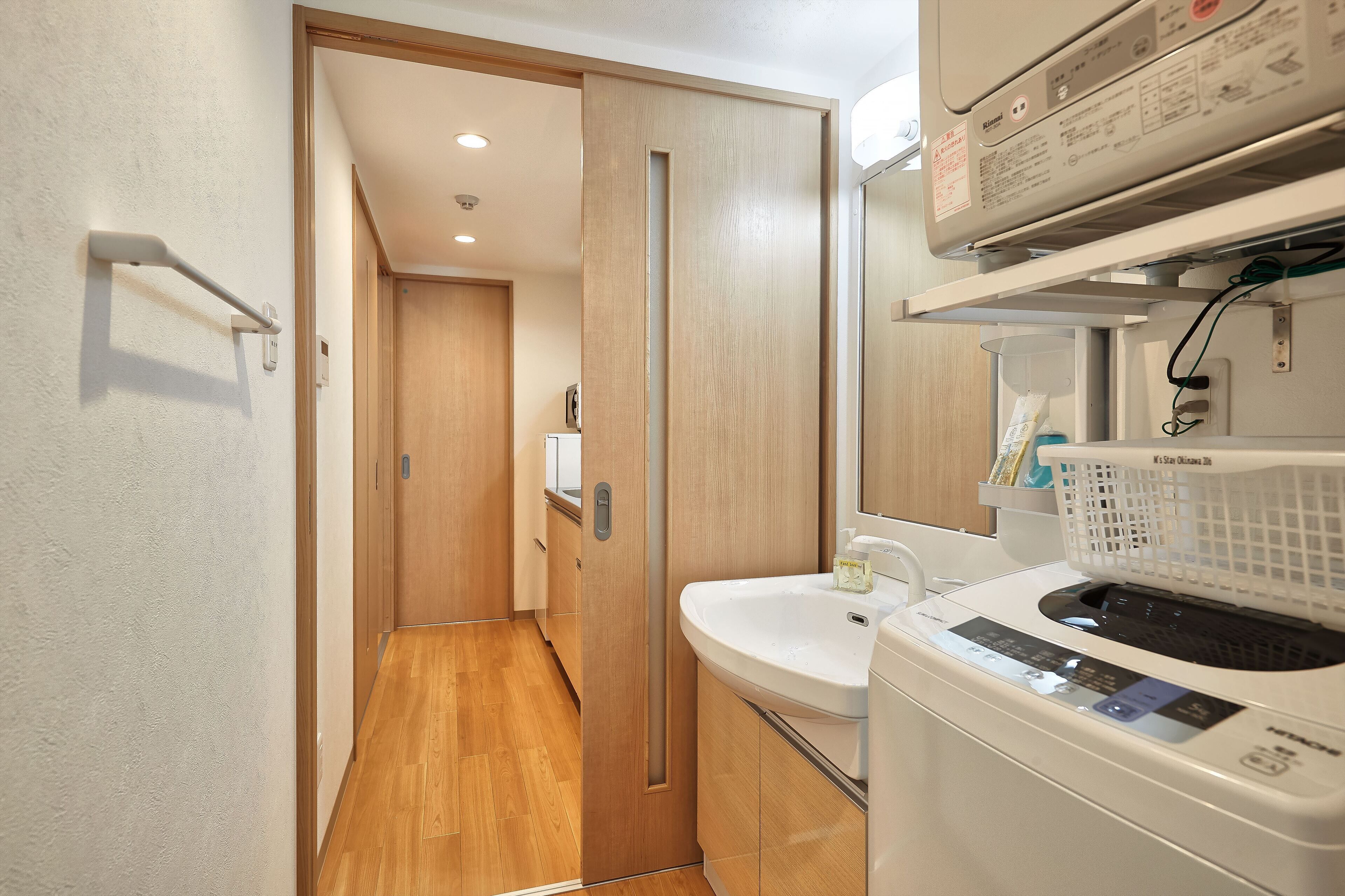 A compact hotel room with a wooden door, a white sink, and a washing machine.