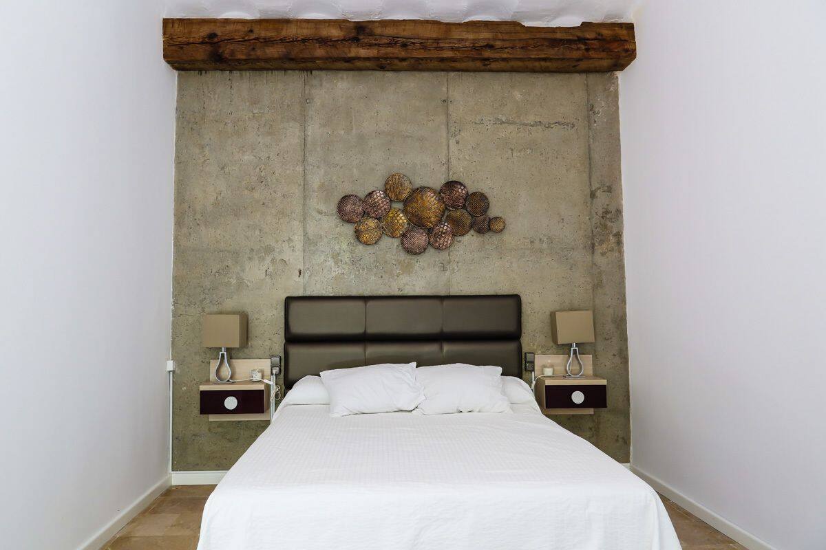 A bedroom with a large bed, two bedside tables, and a headboard with a textured wall behind it.