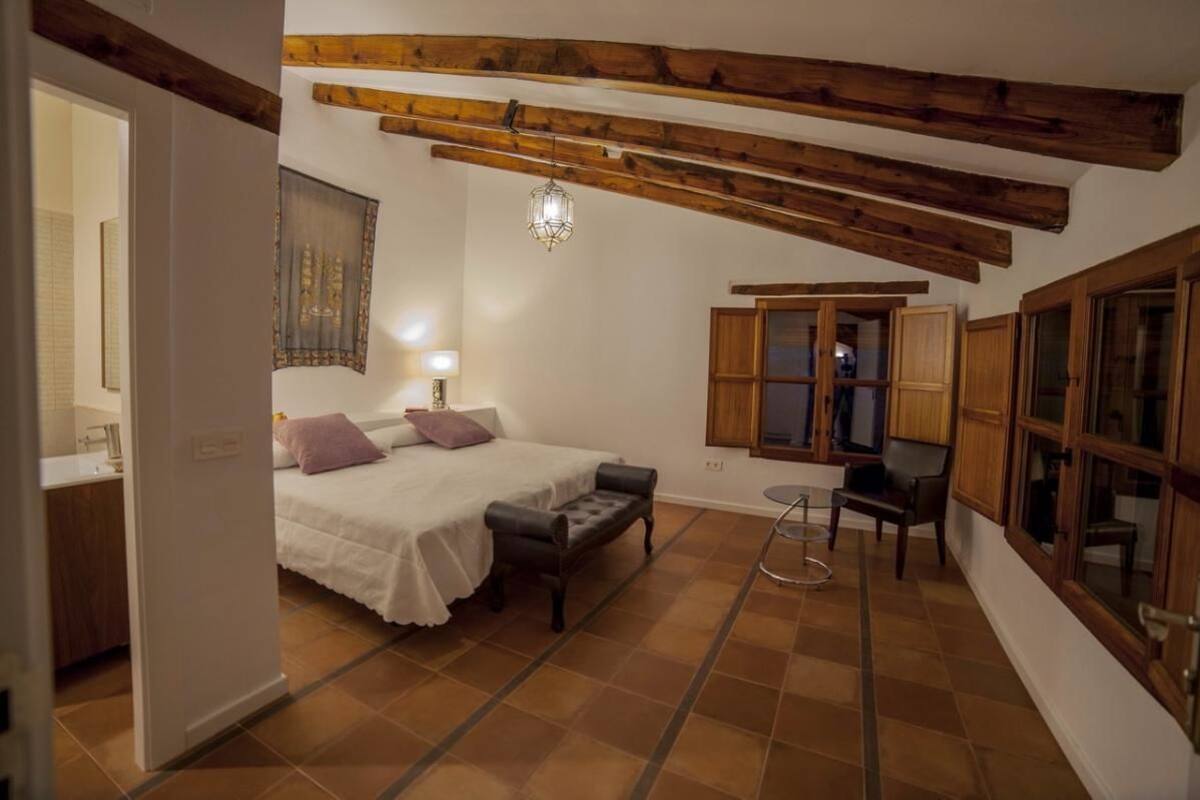 A bedroom with a bed, a bench, a chair, a small table, and wooden beams on the ceiling.