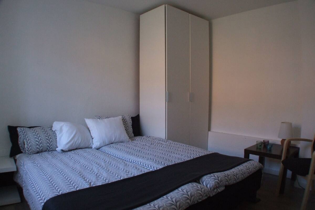 A bedroom with a bed, a wardrobe, a bedside table, and a chair.