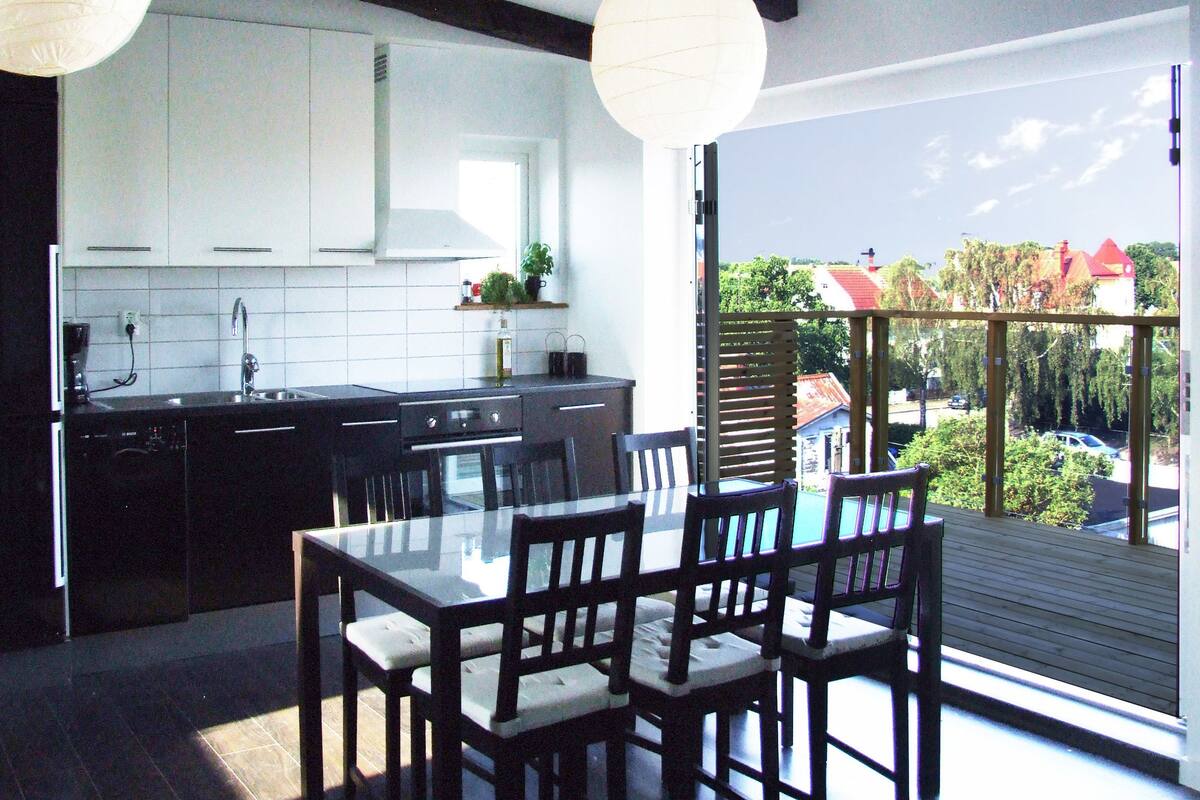 A modern kitchen with white cabinets, a black countertop, and a dining area with a glass table and wooden chairs.