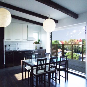 A modern kitchen with white cabinets, a black countertop, and a dining area with a glass table and wooden chairs. - Villa Nore (Borgholm)