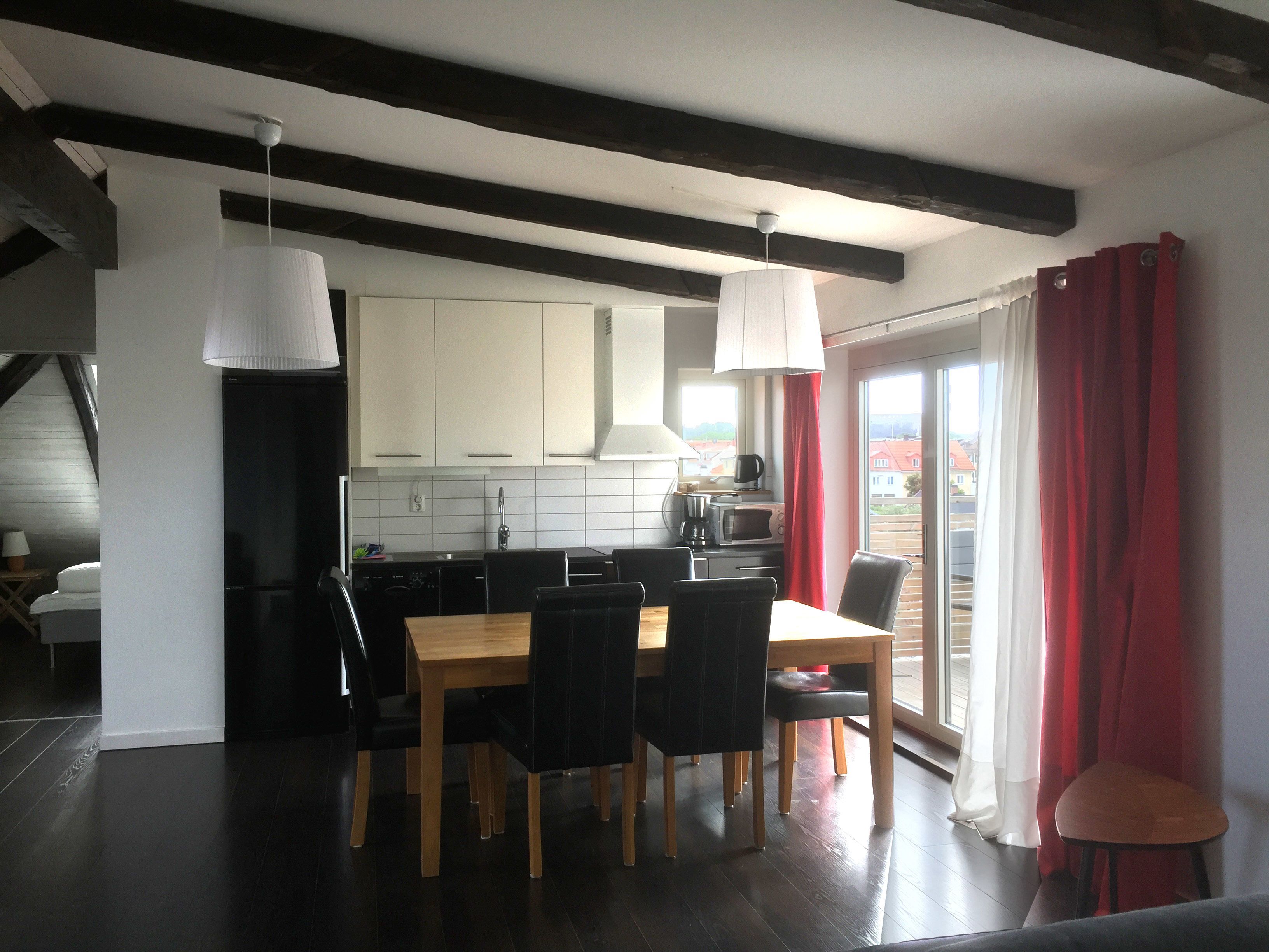 A modern kitchen with white cabinets, a dining area with a wooden table and chairs, and a view of the outside through large windows.
