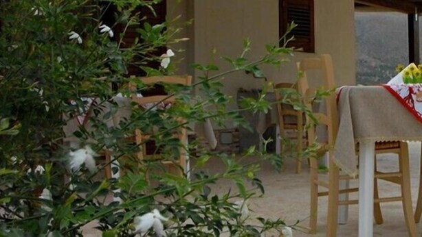Un área de comedor al aire libre con mesas y sillas de madera, cubiertas con manteles, frente a un paisaje montañoso.
