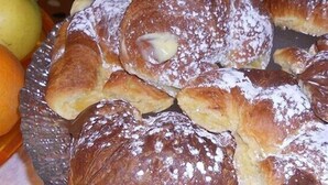 Un plato de pasteles espolvoreados con azúcar glas, acompañado de una naranja y una hogaza de pan.