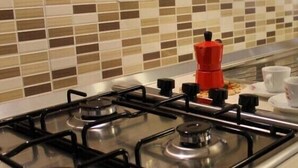 Una cocina con estufa a gas, pileta y salpicadero de azulejos.