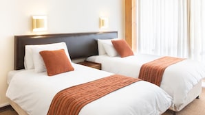 A hotel room with two beds, each with white linens and brown throw pillows. There are wall-mounted lights above the beds and a window with sheer curtains. - Elgro Hotel (Potchefstroom)