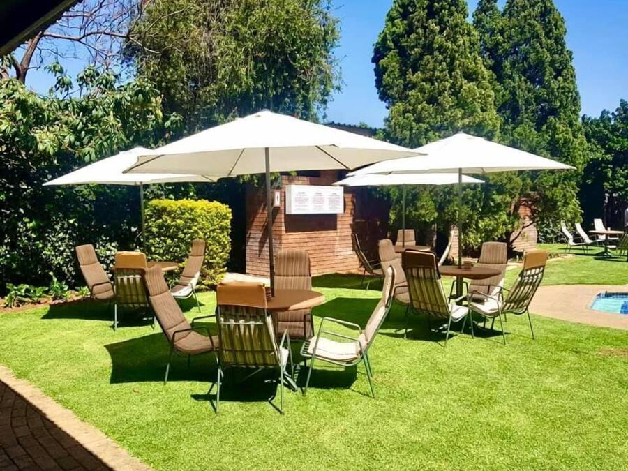 An outdoor seating area with tables and chairs, umbrellas, and a brick wall with a sign.