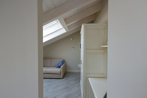A room with a sloped ceiling, a beige sofa, a white cabinet, and a skylight. - San Lorenzo Apartments (Sirmione)
