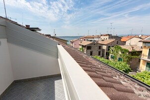 Un balcone con pavimento piastrellato, affacciato su una zona residenziale con edifici in pietra e cielo sereno.