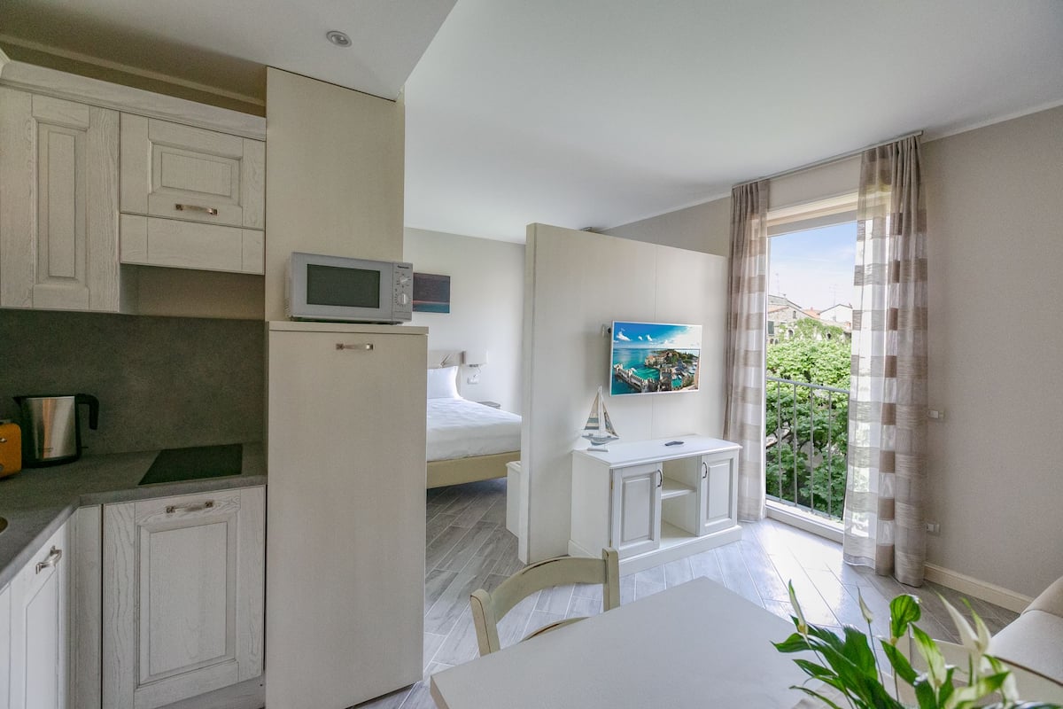 A compact kitchen with a microwave, a small refrigerator, and a coffee maker. There is a dining area with a table and chairs, and a window with a view of greenery.