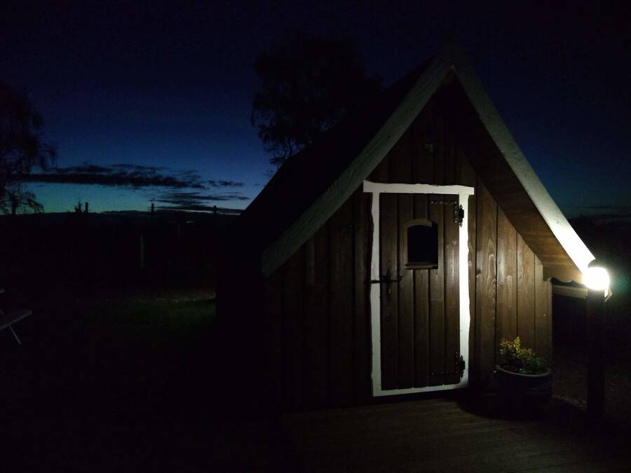 A wooden cabin with a white door and a small window, illuminated by a single light source.
