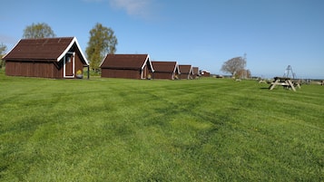 A row of wooden cabins with sloped roofs, set in a grassy field with trees in the background.