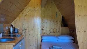 A compact wooden cabin with a kitchenette, a bed with blue bedding, and a small wooden table. - Macbeth's Hillock (Nairn)