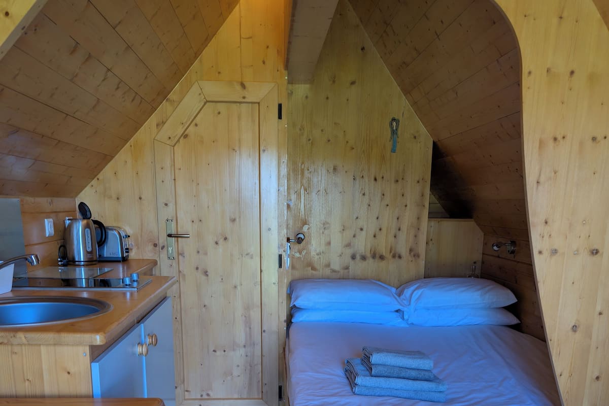 A compact wooden cabin with a kitchenette, a bed with blue bedding, and a small wooden table.