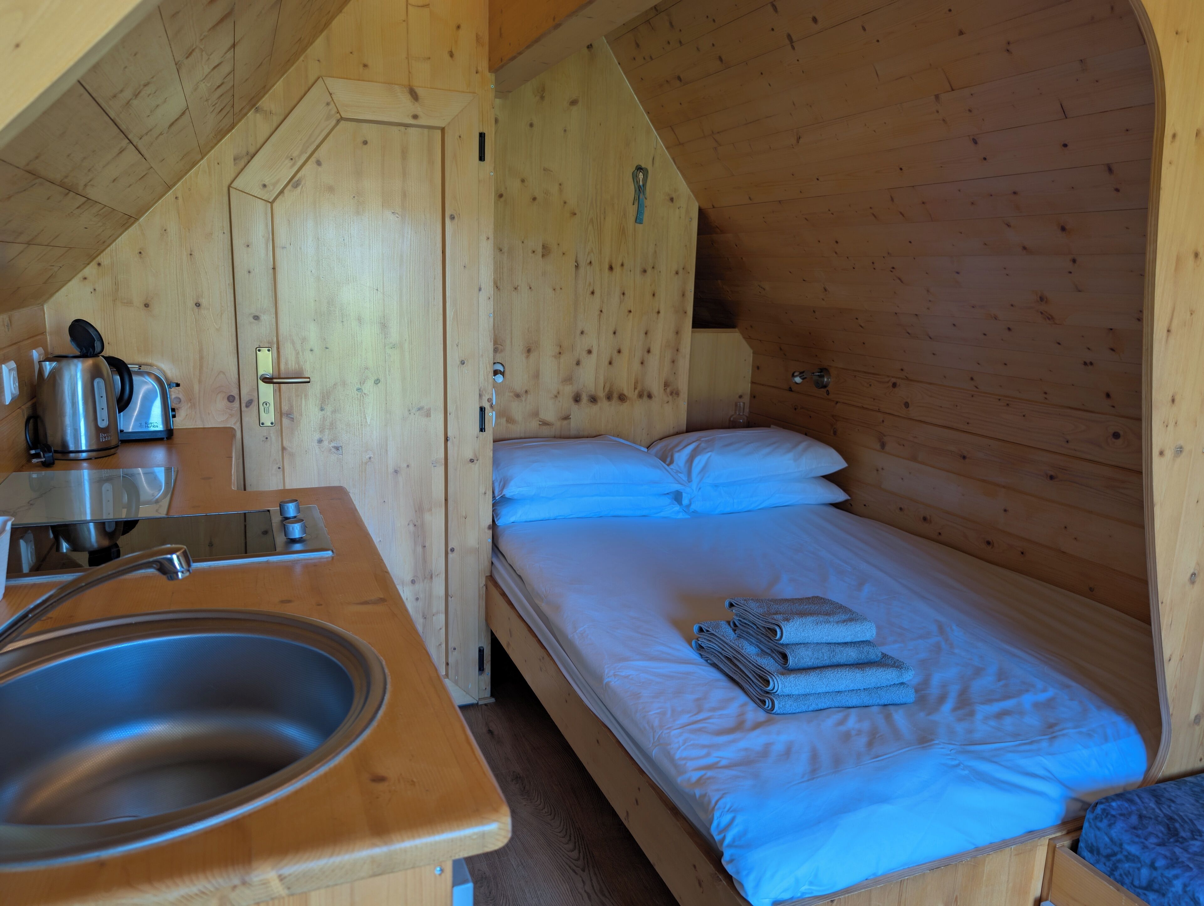 A wooden cabin room with a bed, a sink, and a kettle.