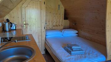 A wooden cabin room with a bed, a sink, and a kettle.