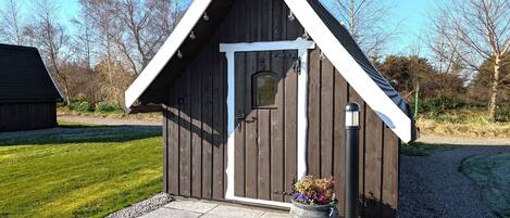 Une petite cabane en bois avec une porte blanche et un toit triangulaire.