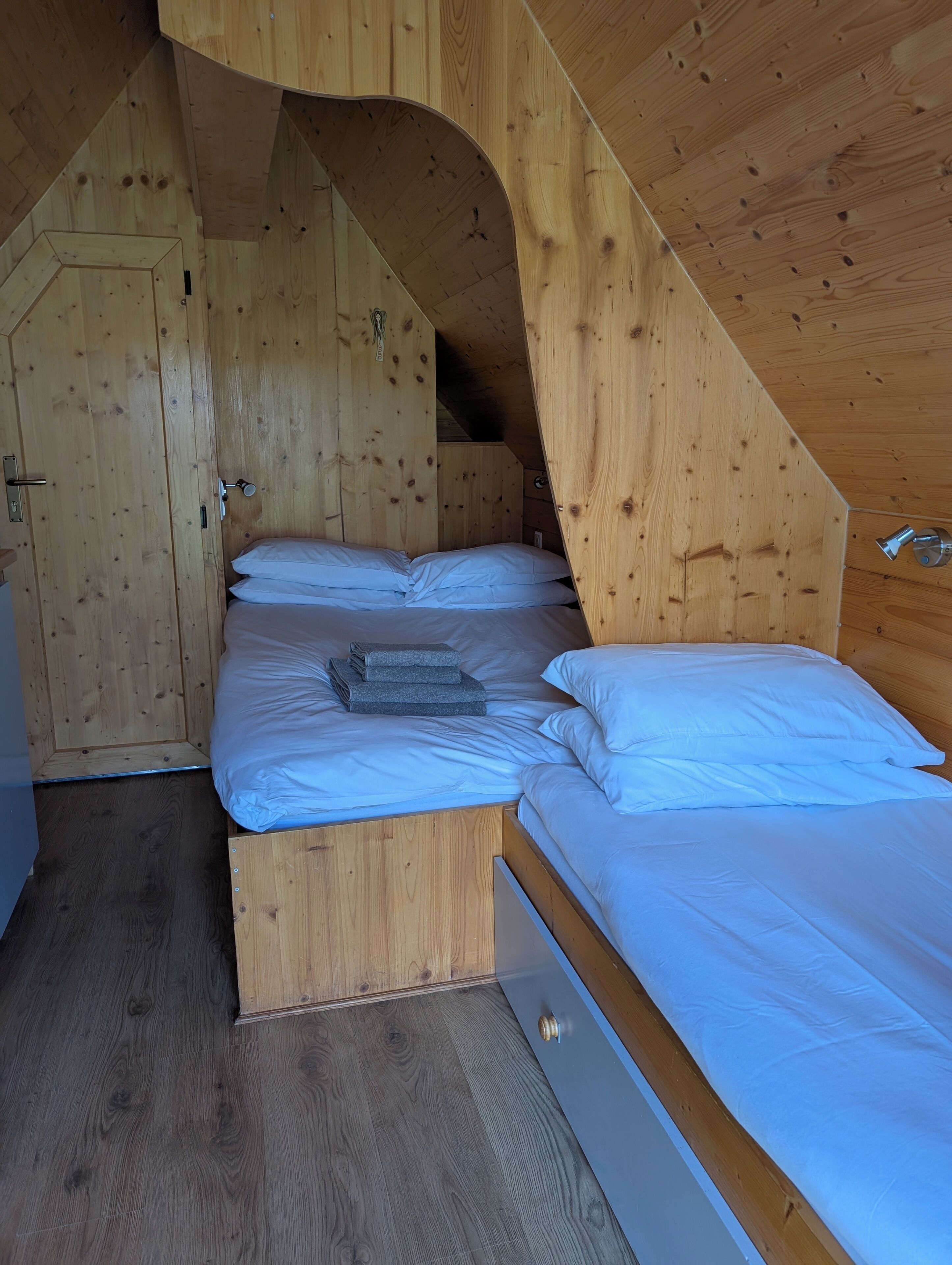 A wooden bunk bed with white bedding, a wooden wardrobe, and a sloped ceiling.